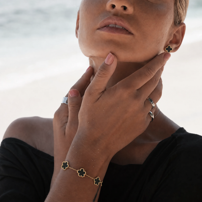 Trèfle Bracelet Gold & Onyx worn on model wrist, beach lifestyle shot with hands raised to chin