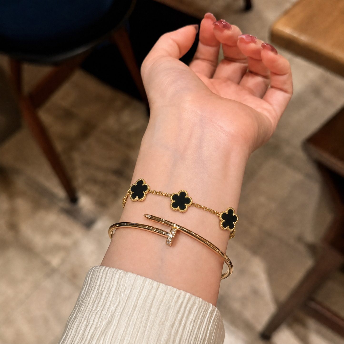 Trèfle Bracelet Gold & Onyx black clover bracelet on wrist stacked with gold tone bangle, indoor shot