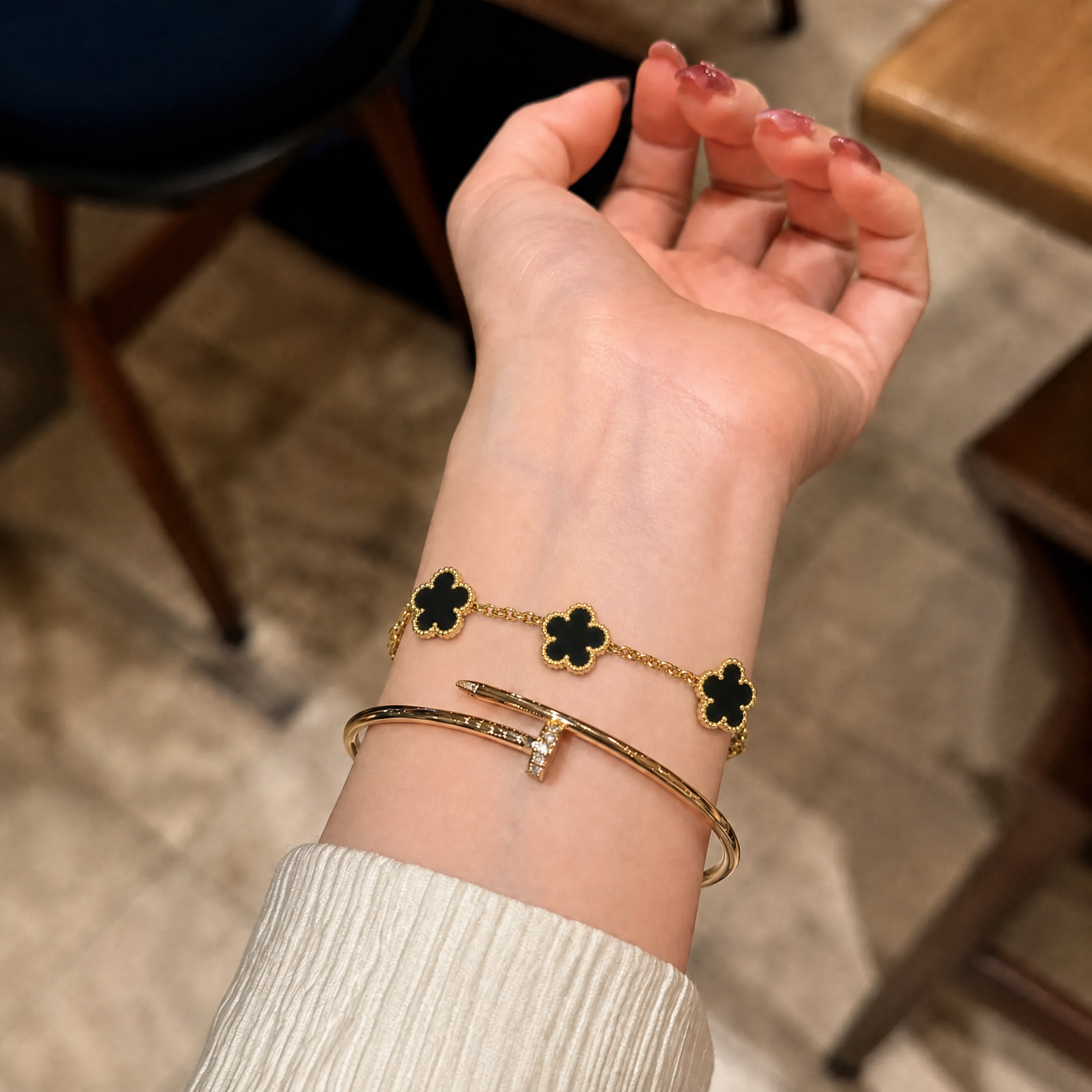 Trèfle Bracelet Gold & Onyx black clover bracelet on wrist stacked with gold tone bangle, indoor shot